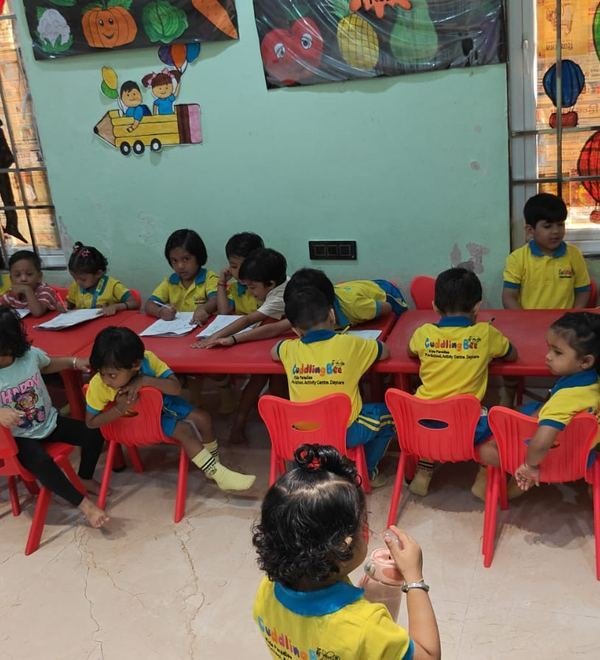 Children gathered around red classroom tables during a writing activity